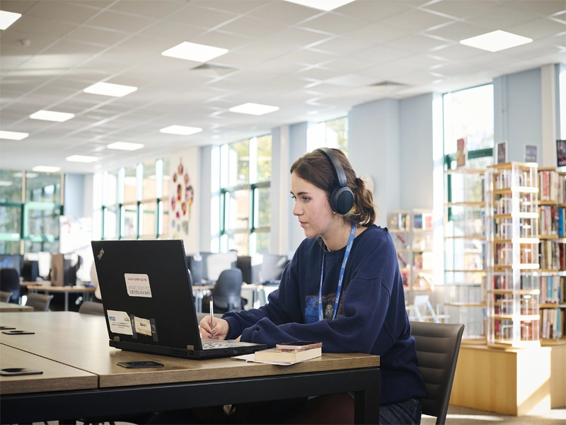 Close up of female student working in library on laptop