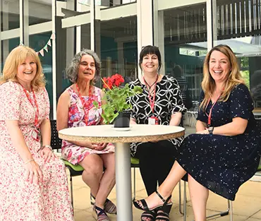 Four higher education teachers smiling, sat around a table in courtyard