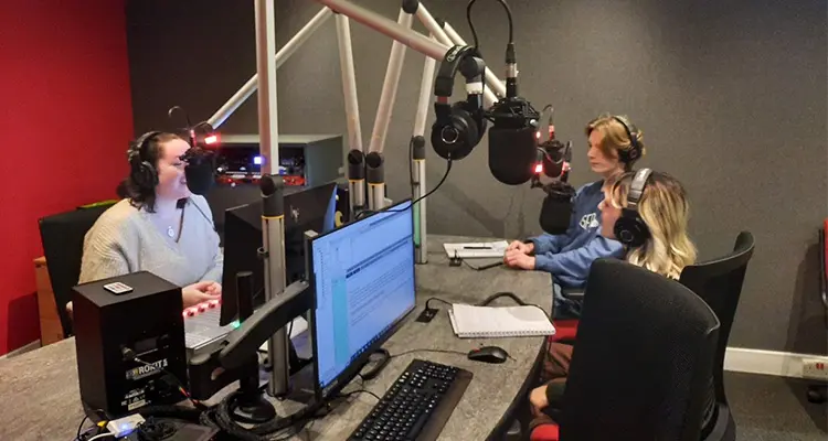 Students in a podcast room, talking into microphones