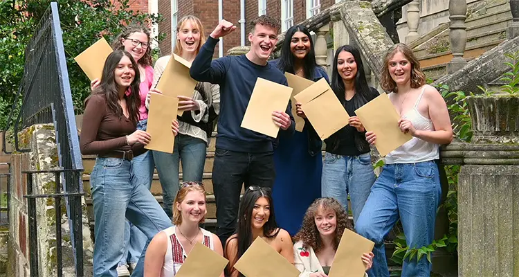 A group of students all cheering and holding brown envelopes with their results in them