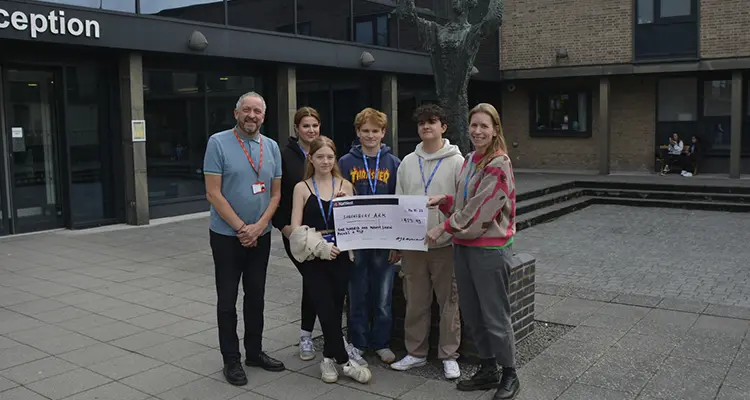 Group of students standing with staff member holding a cheque outside London Road Campus