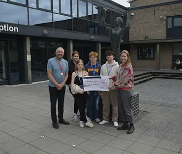 Group of students standing with staff member holding a cheque outside London Road Campus