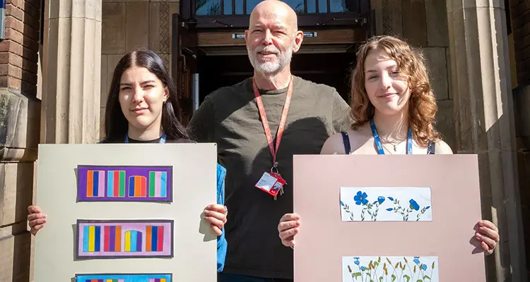 Two students holding up art work with art teacher in the middle