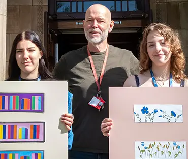 Two students holding up art work with art teacher in the middle