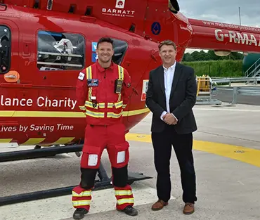 College principal and midlands air ambulance representative standing in front of helicopter smiling