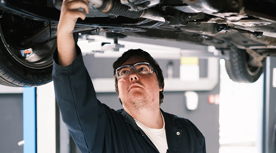 student in overalls examining underside of car