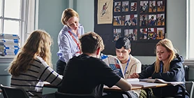 Students around a desk with teacher reading book