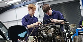 Two young students investigating a car engine